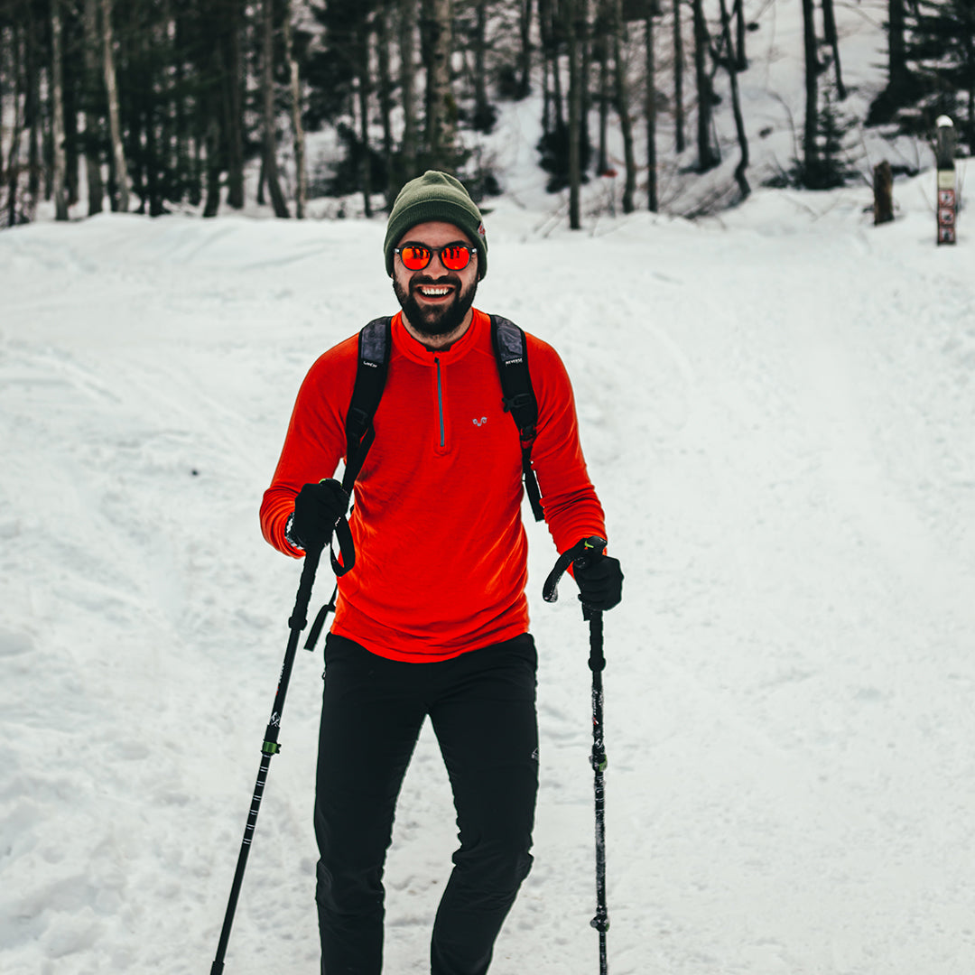 Skifahrer trÀgt Merino-Langarmshirt von Woolona in der Farbe Orange, lÀchelt und fÀhrt Ski.