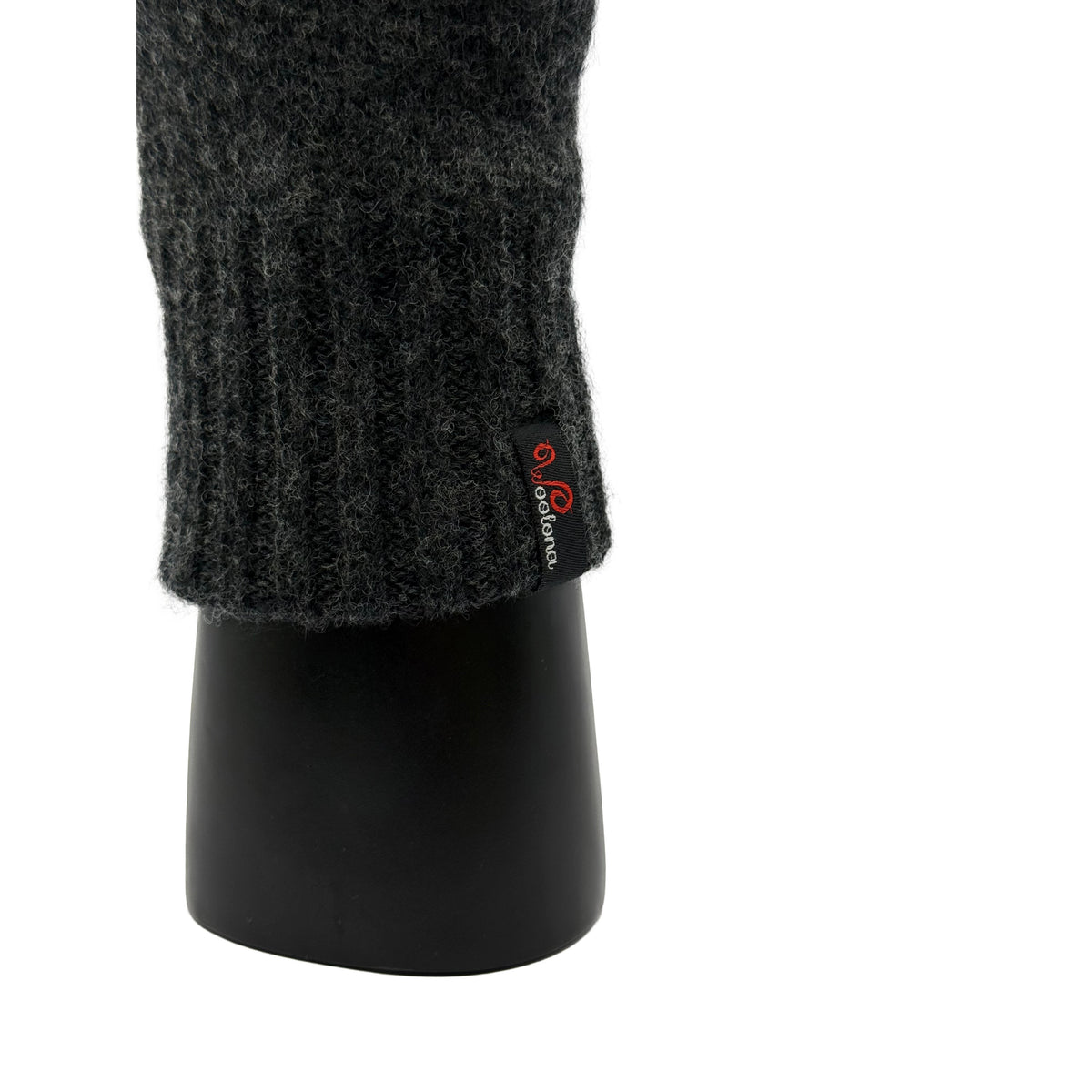 Aus der nähe eine Hand die ein Handschuh aus Merinowolle in Anthrazit trägt und das Woolona Logo zeigt