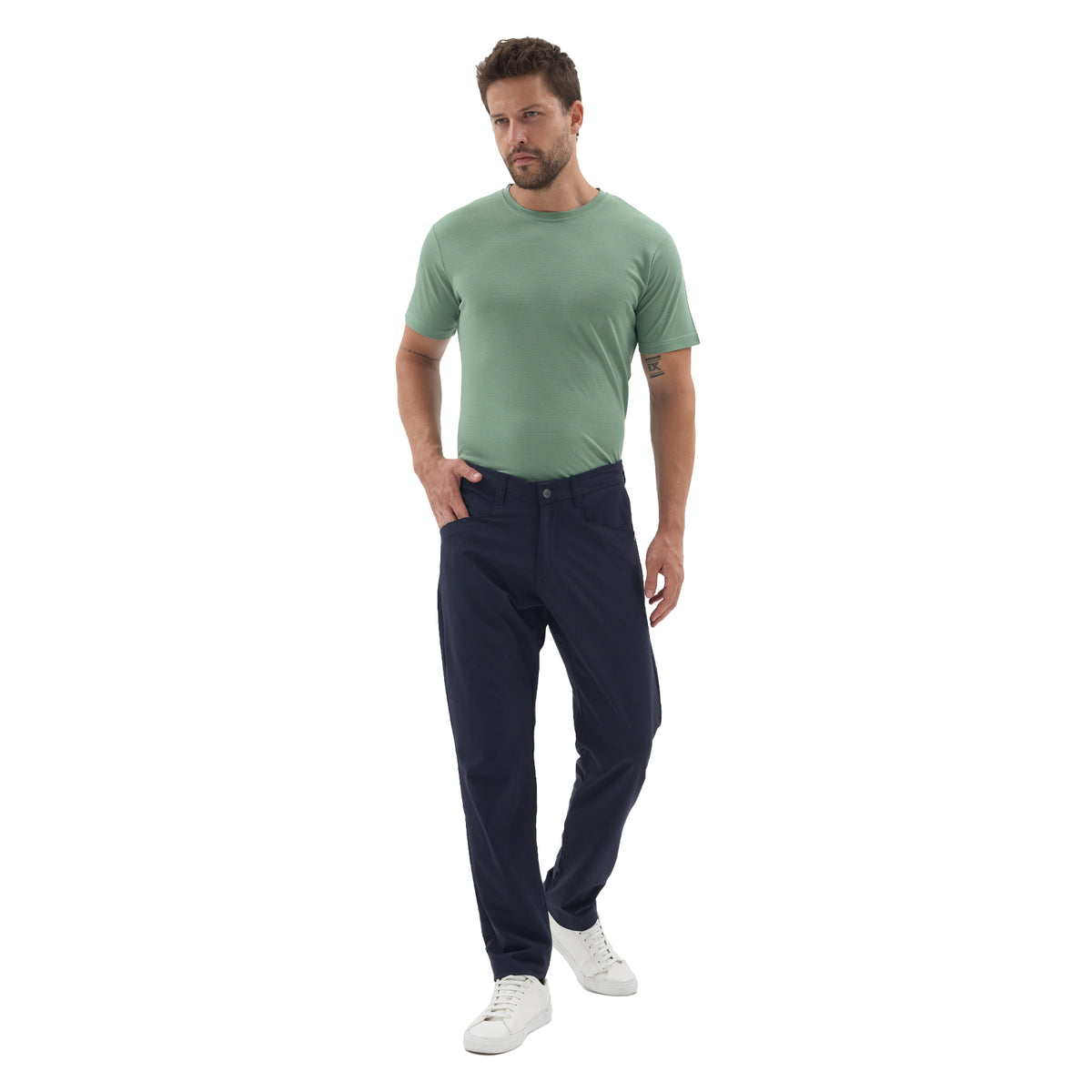 Mann mit grünem Merinoshirt und einer Travelhose aus Merinowolle in der Farbe navy mit Hosentaschen. 