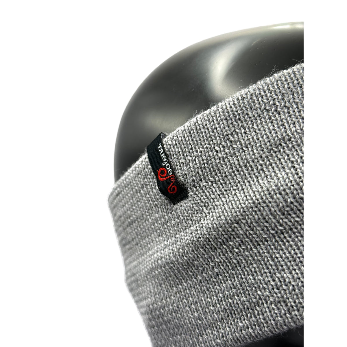 Ein Puppenkopf aus der nähe das ein Stirnband aus Merino in Grau trägt mit dem Woolona Logo