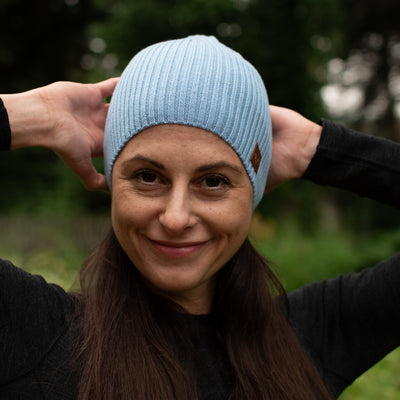 Frau mit einer hellblauen Merinomütze in der Natur. 