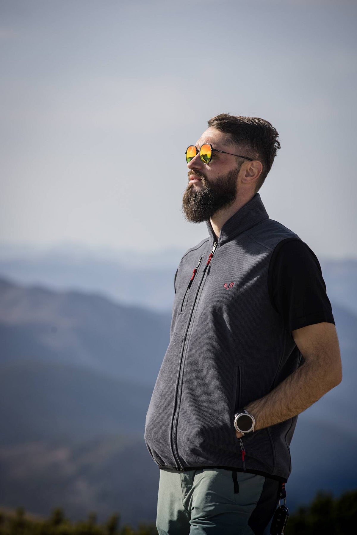 Ein Mann mit Sonnenbrille trägt eine Merinoweste und er blickt in die Ferne